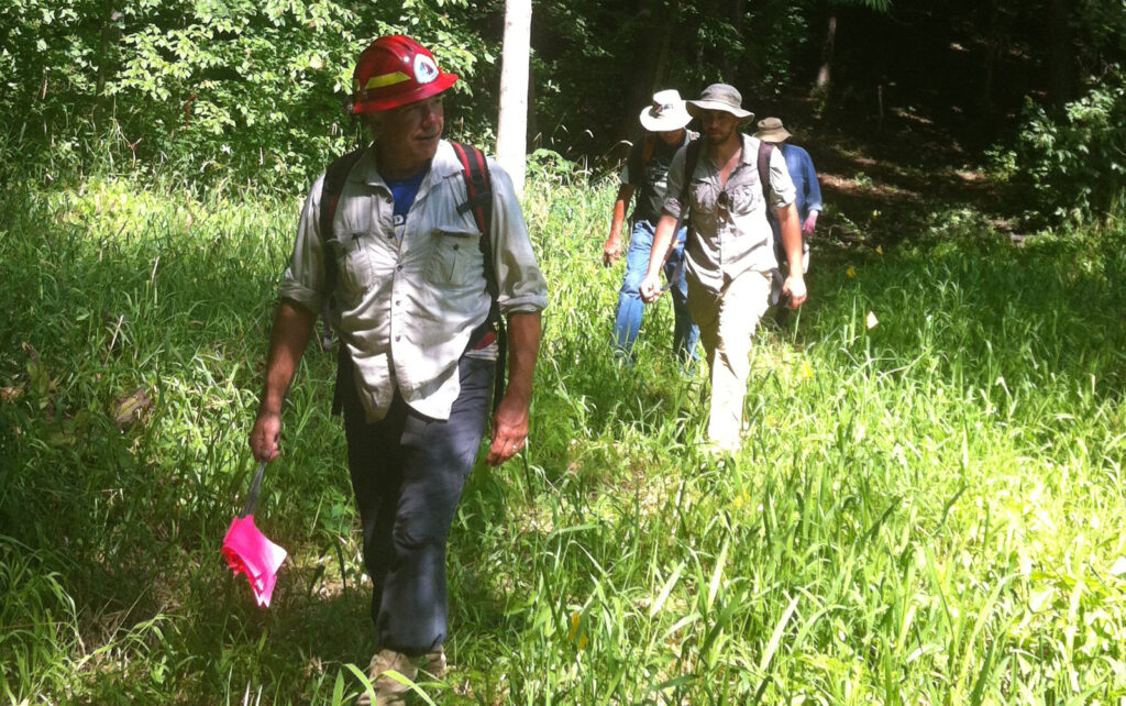 Volunteers wearing field clothes and hats walking up a grassy path.