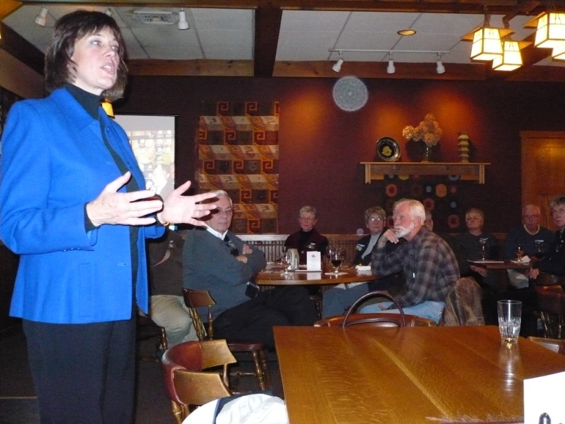 A middle aged woman in a blue suit jacket talking to people in a small town bar.