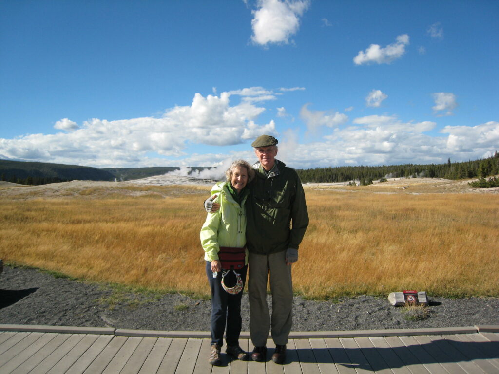 An older couple standing with their arms around each other on a boardwalk in a large natural area.