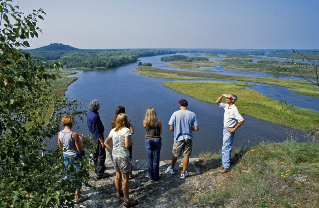 Several people standing on a bluff looking out over water.