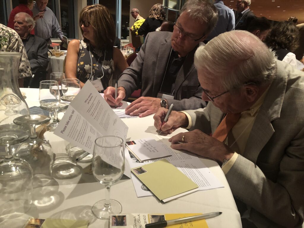 People sitting around a banquet table signing letters.