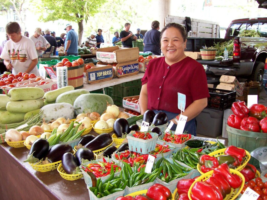 An Asian woman selling produce at a farmers market.