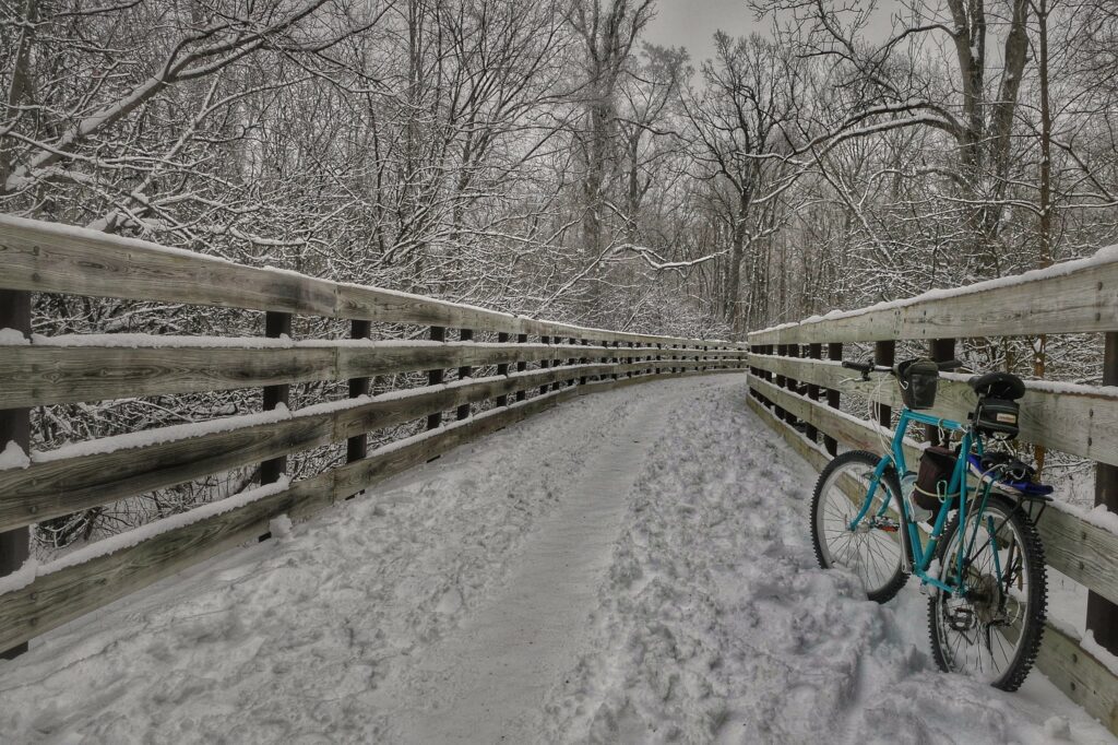 A bicycle leaning up against the railing of a snow-covered bridge in winter.