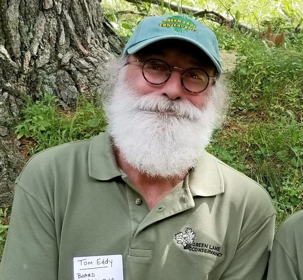 An older man with a white beard and green baseball hat in front of a tree.
