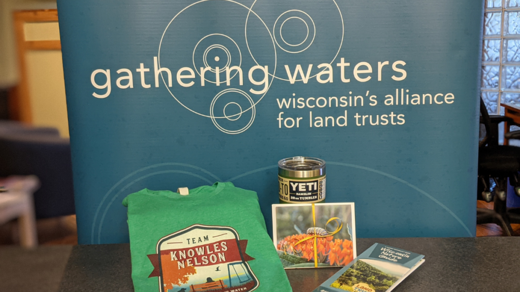 A t-shirt, YETI tumbler, set of cards, and nature guide on a counter with a Gathering Waters banner behind.