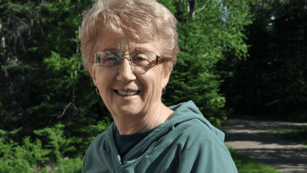 An older woman wearing glasses and a green sweatshirt posing for a picture outside.