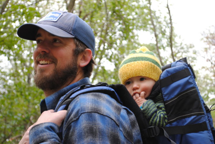 Adult wearing a hat and flannel carrying a child wearing a beaning