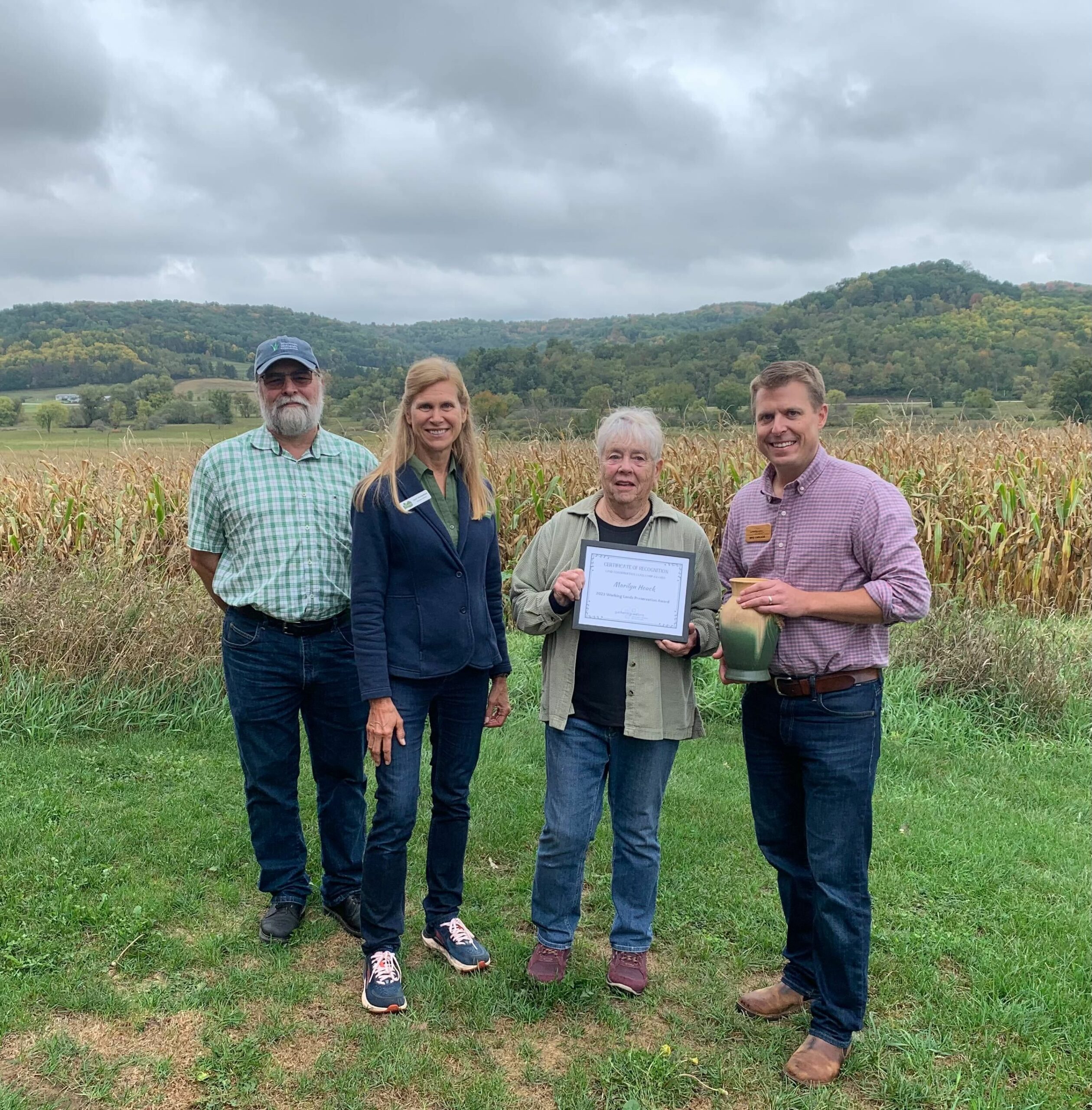 Four adults standing outside in a field on a cloudy day for an award presentation.