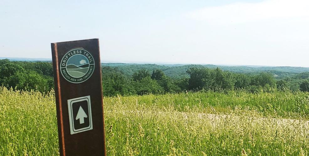 A trail marker for the Driftless Trail and a large field in summer.