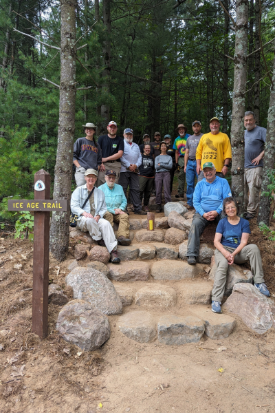 A group of people sitting on the concrete steps of a nature trail next to an Ice Age Trail signpost.