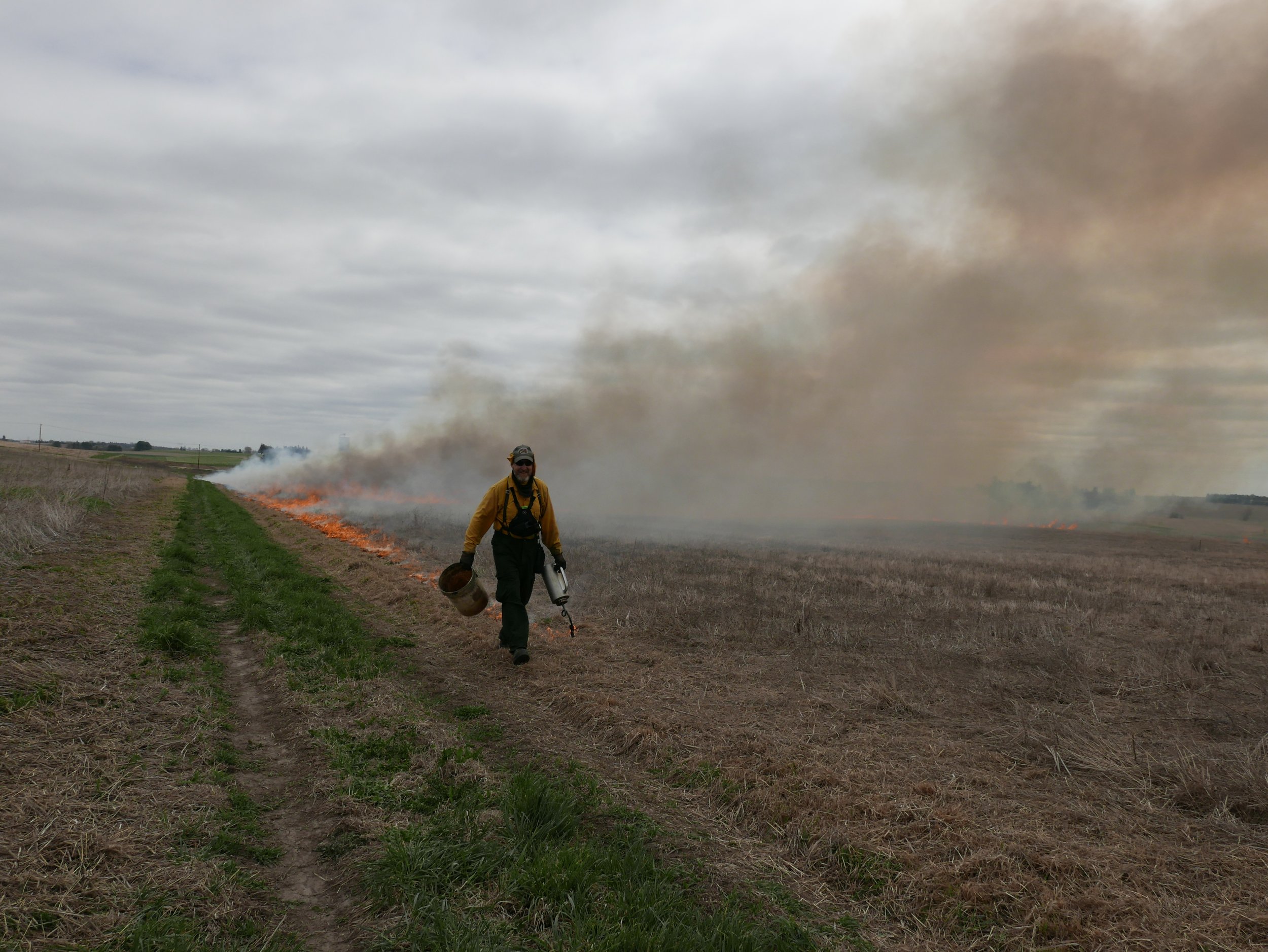 A man in fire safety gear burning a field during a prescribed burn.