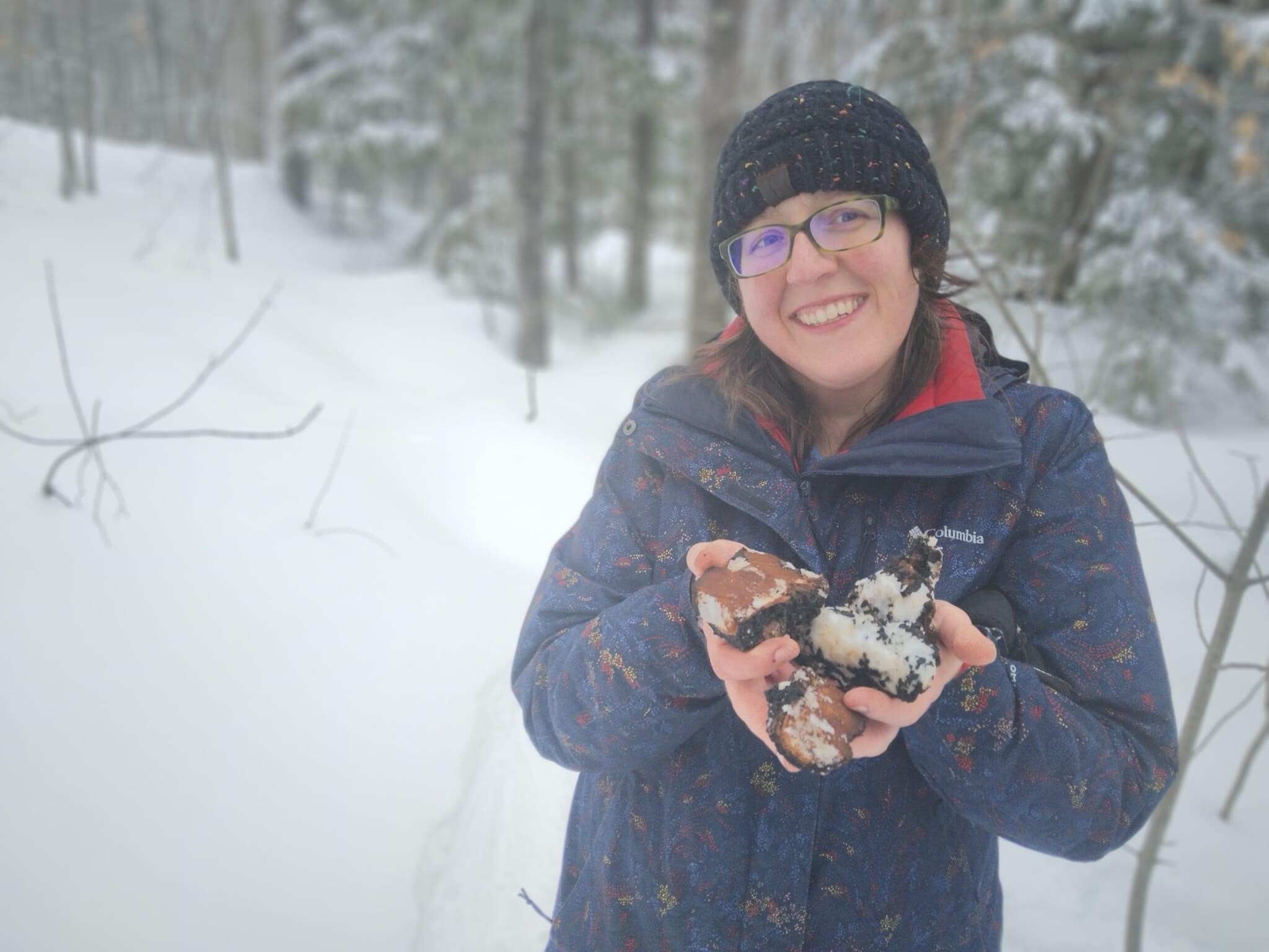 A photo of educator Crystal Brown holding foraged mushrooms in a snowy forest.
