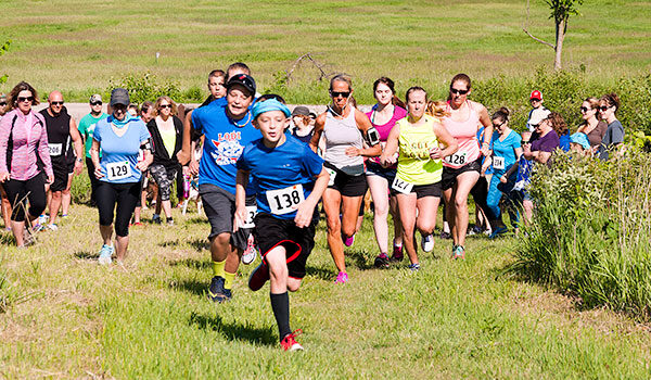 A group of marked runners race up a grassy hill, lead by a young man.