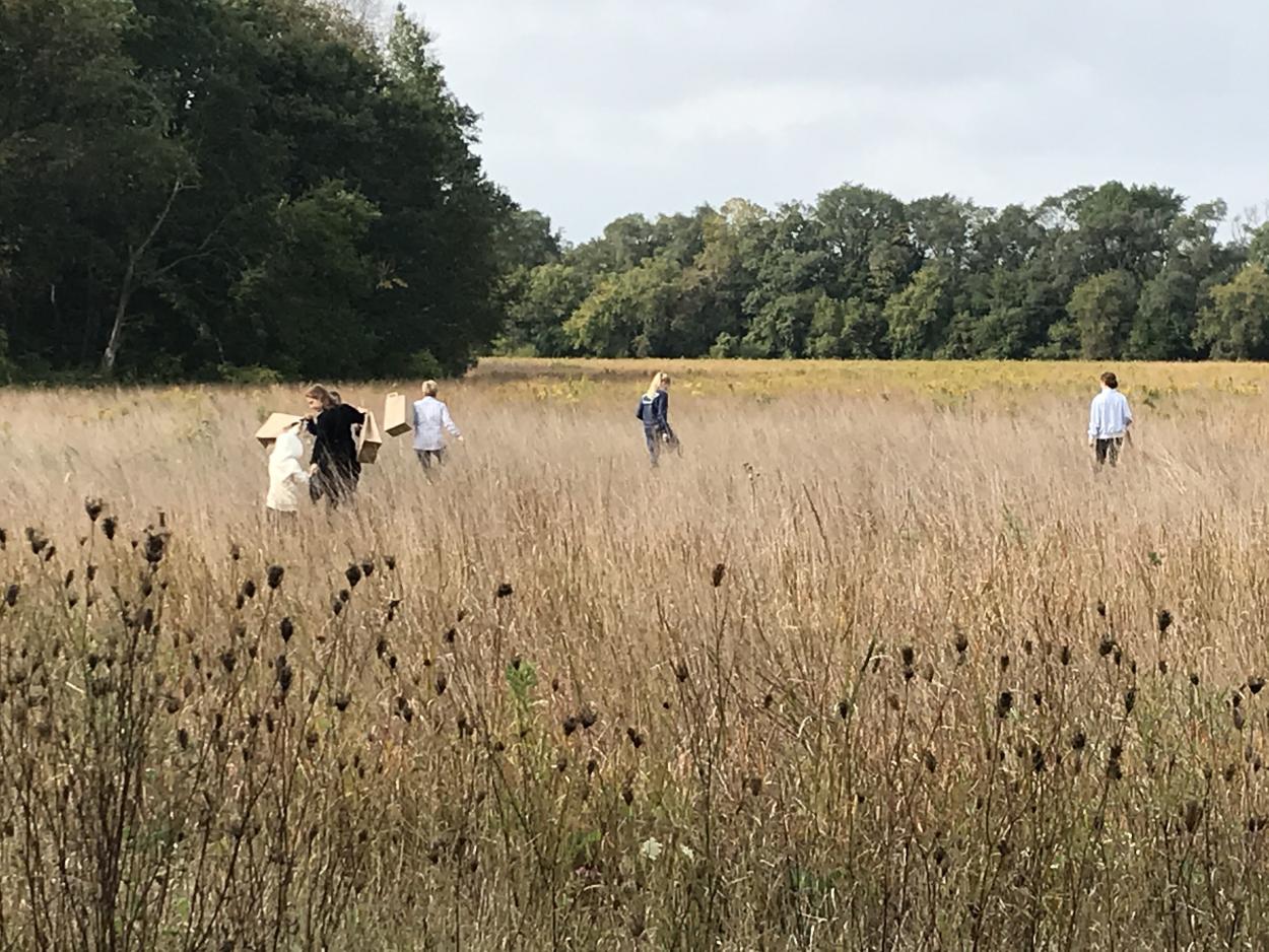 People walking through a prairie carrying bags
