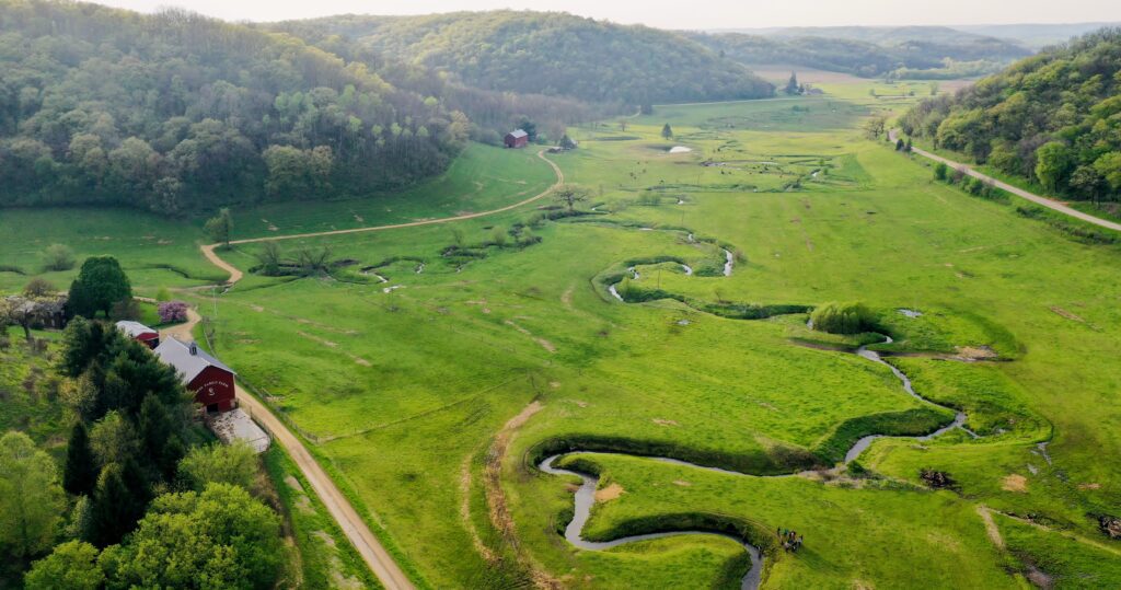 Creek surrounded by green grass, trees, and farm houses