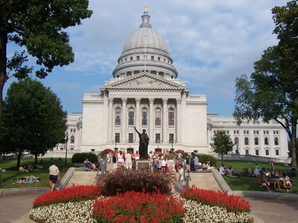 The Wisconsin State Capitol building with people on the steps and red and white flowers.