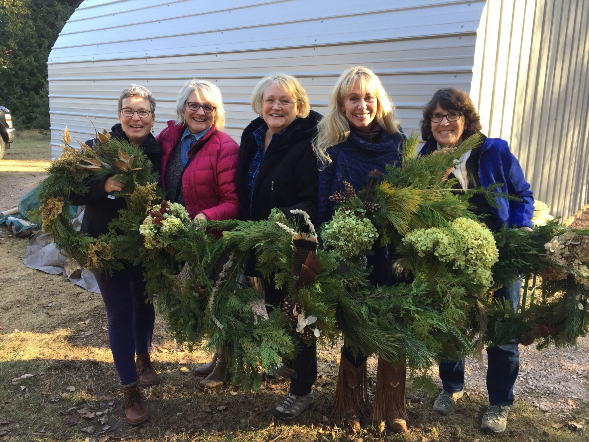 A group of people holding up their finished wreaths after a wreath-making workshop.