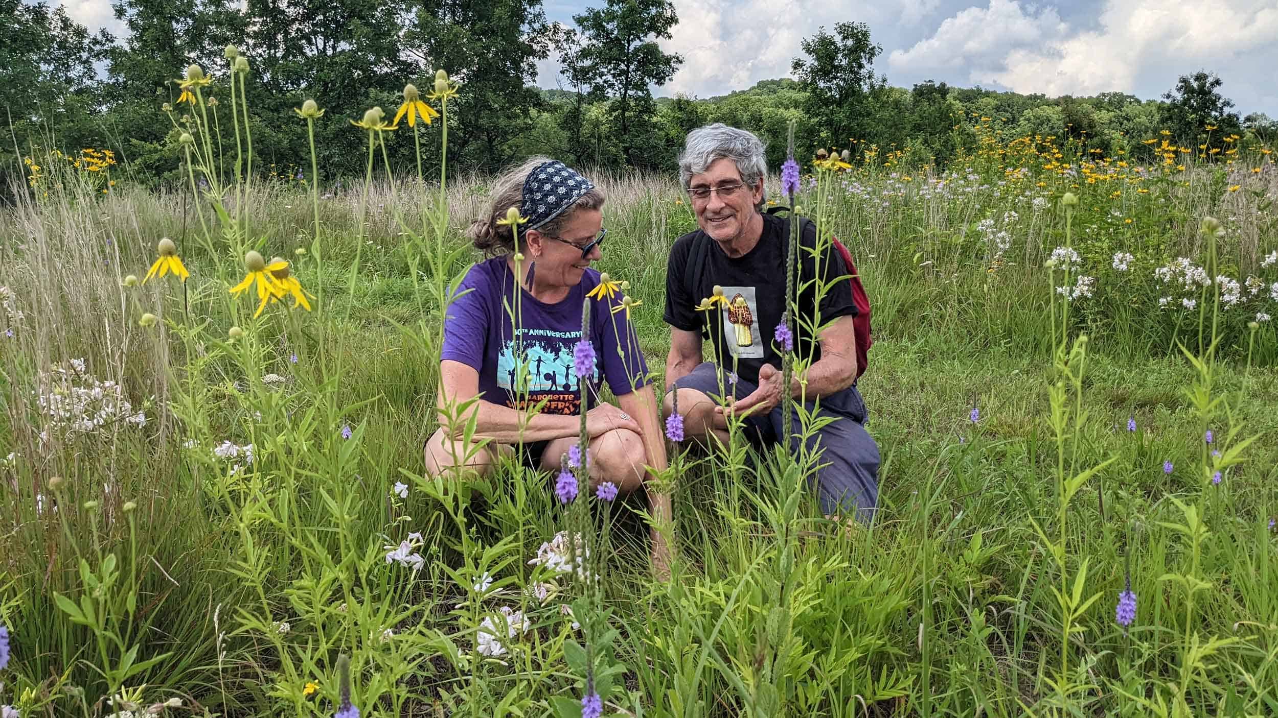 Two people looking at wildflowers in a tall grass prairie.