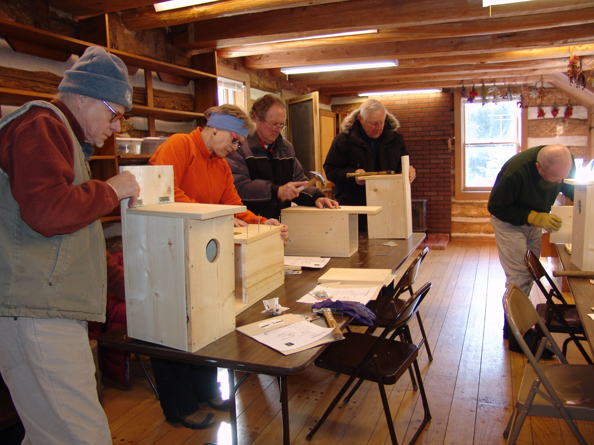 People at tables in a classroom making owl nest boxes.