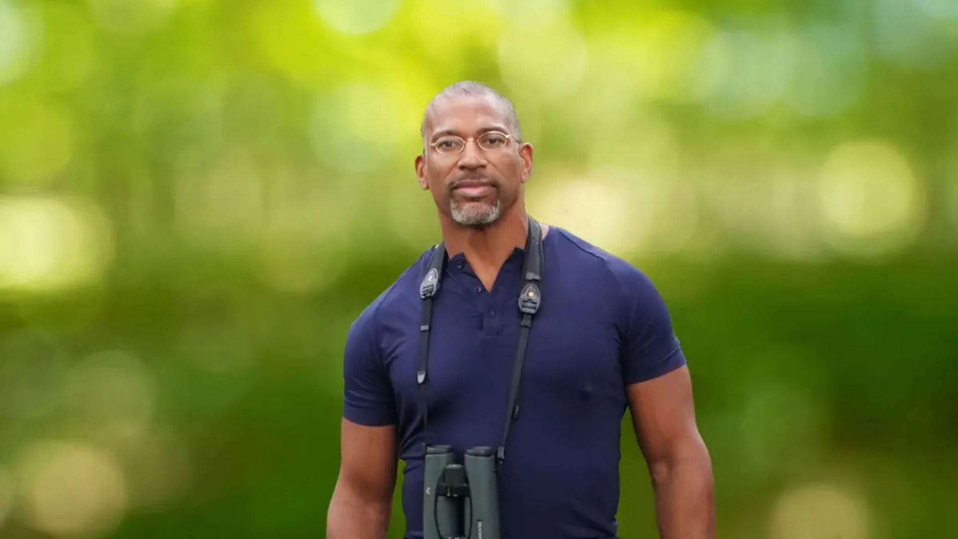 A Black man wearing a dark blue shirt and a large pair of binoculars.